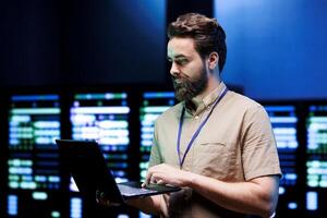 Specialist using laptop to do scans on blade servers in data storage facility. Cloud computing computer service business used for complex calculations and massive datasets processing photo