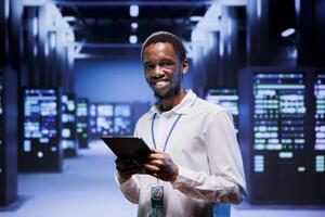 Portrait of engineer in front of operational mainframes in high performance computing server room. Specialist monitoring equipment energy consumption, ensuring ideal operations conditions photo