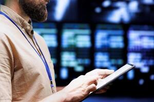 Professional using tablet to check technologically advanced data center security features protecting against unauthorized access, data corruption, DDoS attacks and other cybersecurity threats photo