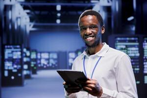 Portrait of smiling technician in front of supercomputers in high performance computing server room, ensuring flawless operations conditions. Expert monitoring data center hardware energy consumption photo
