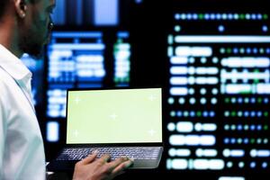 Developer examining server rigs performance trends using chroma key device. Expert using green screen laptop to discover data center damage troubles arising due to high CPU usage photo