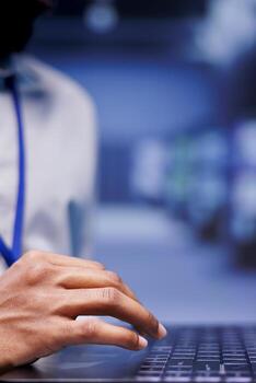 IT administrator investigating servers in blurry background delivering web content to customers. Adept serviceman using laptop to make sure critical systems are working properly, close up photo