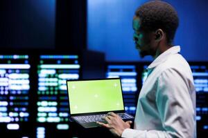 Engineer using green screen laptop to do hardware maintenance in professional data center. Expert optimizing server room equipment, ensuring seamless data operations and system stability photo