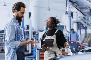 Repairman in car service orders new engine for damaged vehicle using laptop. Knowledgeable engineer next to customer looking online for components to replace old ones in malfunctioning automobile photo