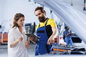 Technician at auto repair shop conducts annual vehicle checkup, informing client about needed engine replacement. Skillful garage worker talks with customer after finishing car inspection photo