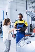 Mechanic in car service orders new fuel tank for damaged vehicle using laptop. Skilled technician next to customer looking online for components to replace old ones in malfunctioning automobile photo