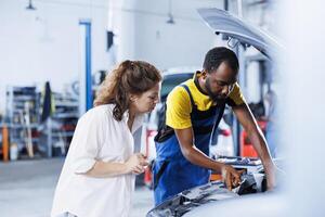 Engineer at auto repair shop conducts annual vehicle checkup, informing client about needed engine replacement. Diligent garage worker talks with customer after finishing car inspection photo