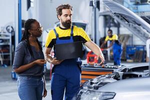 Mechanic in car service ordering new radiator for damaged vehicle using laptop. Qualified technician next to customer looking online for components to replace old ones in malfunctioning automobile photo
