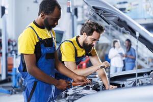 Coworkers using oil extractor tool to change old depleted brake fluid with new one in auto repair shop. BIPOC mechanic and colleague using professional equipment to do car maintenance photo