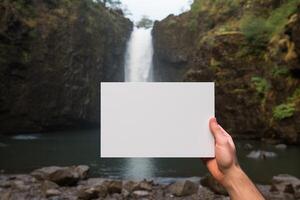 A person standing in front of a waterfall, holding a card in their hand. photo