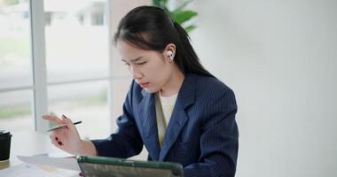 Footage dolly shot, Asian businesswoman in suit use digital tablet for work and analyze documents in small coffee shop. Work from anywhere, Remote working video