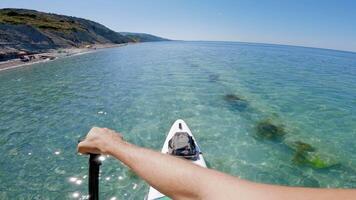 Men rowing on SUP board on quiet transparent sea. First person view of stand paddle boarding in summer. video