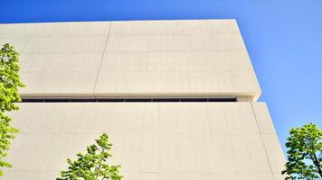Modern white concrete building walls against blue sky. Eco architecture. Green trees and concrete office building. The harmony of nature and modernity. photo