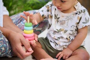Details on a colorful wooden pyramid for education and developing motor skills. Adorable baby boy showing curiosity and interest to learning colors and texture of educational games. Babyhood concept photo