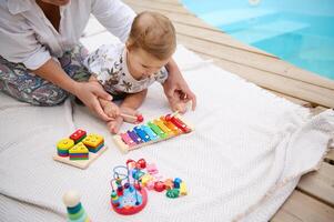 Mother and baby playing with colorful educational toys by the pool photo