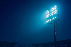 Bright stadium floodlights illuminating a sports field at night against a dark blue sky, creating a dramatic and vibrant atmosphere. photo