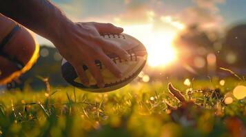Hand touching a football during a sunset on a grassy field, capturing the essence of sports and evening practice. photo