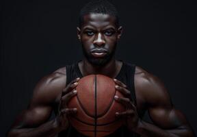Determined basketball player holding a ball in a dark, dramatic setting. Focus and intensity are evident on his face and muscular build. photo