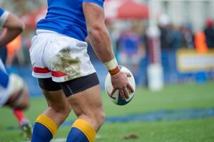 Rugby player holding the ball on a green field, prepared to make a move during an intense match, focusing on athleticism and strategy. photo