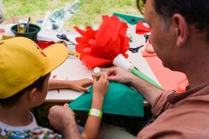 Father and son are engaged in creativity together. Dad spends time with his son cutting out large red flowers from paper photo