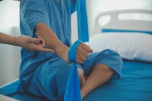 Close up hand patient doing stretching exercise with a flexible exercise band and a physical therapist hand to help in clinic room. photo