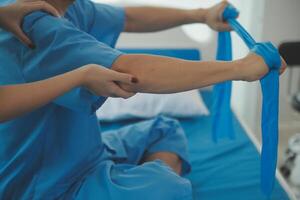 Close up hand patient doing stretching exercise with a flexible exercise band and a physical therapist hand to help in clinic room. photo