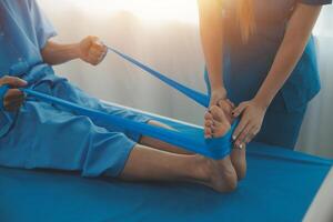 Professional orthopedist examining the little patient's leg in the clinic. Patient at the physiotherapy doing physical exercises with his therapist photo