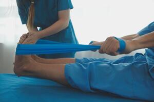 Professional orthopedist examining the little patient's leg in the clinic. Patient at the physiotherapy doing physical exercises with his therapist photo