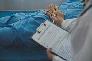 Hospitalized man lying in bed while doctor checking his pulse. Female physician examining male patient in hospital room. photo