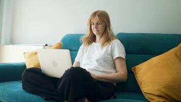 Happy 30s woman making call on laptop while relaxing on a sofa having pleasant conversation waving hand greeting gesture smiling to laptop screen video
