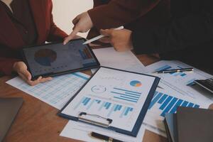 Group of confident business people point to graphs and charts to analyze market data, balance sheet, account, net profit to plan new sales strategies to increase production capacity. photo