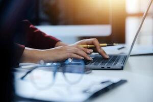 Cropped image of professional businesswoman working at her office via laptop, young female manager using portable computer device while sitting at modern loft, flare light, work process concept photo