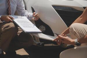 Side view of writing on clipboard while insurance agent examining car after accident photo