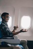 Asian man enjoying enjoys a coffee comfortable flight while sitting in the airplane cabin, Passengers near the window. photo