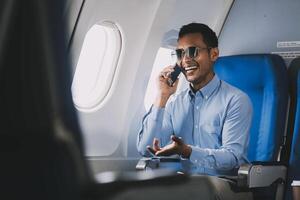 Traveling and technology. happy young businessman working on laptop computer and smartphone while sitting in airplane. photo
