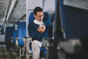 Man with dark hair is reading text message on mobile phone and speaking by phone during flying in the airplane photo