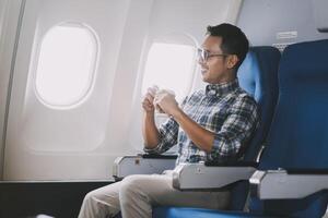 Asian man enjoying enjoys a coffee comfortable flight while sitting in the airplane cabin, Passengers near the window. photo