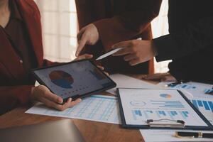 Group of confident business people point to graphs and charts to analyze market data, balance sheet, account, net profit to plan new sales strategies to increase production capacity. photo