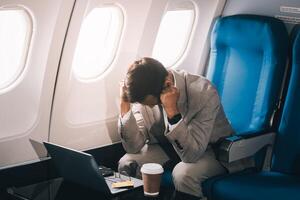 Stressed and professional Asian businessman in a business class, having a serious phone call with someone during the flight to a business meeting. photo