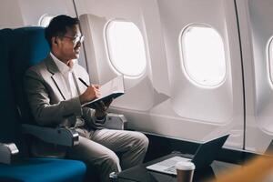 Airplane, travel and portrait of businessman working on laptop computer and smartphone while sitting in airplane. photo