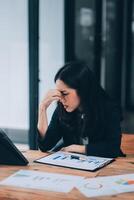 Young sad businesswoman is sitting at table, covering his face On desk is laptop, tablet computer, Stress. Serious woman concentrating on his paper work. photo