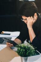 Frustrated Asian young businessman worker working on table in office. Busy employee worker people feel tired and headache from late work and overwork job document on computer desk at company workplace photo
