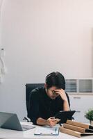 Frustrated Asian young businessman worker working on table in office. Busy employee worker people feel tired and headache from late work and overwork job document on computer desk at company workplace photo