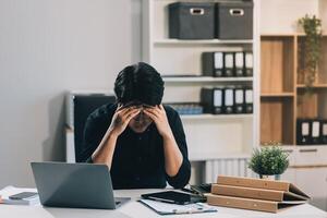 Frustrated Asian young businessman worker working on table in office. Busy employee worker people feel tired and headache from late work and overwork job document on computer desk at company workplace photo