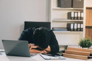 Frustrated Asian young businessman worker working on table in office. Busy employee worker people feel tired and headache from late work and overwork job document on computer desk at company workplace photo