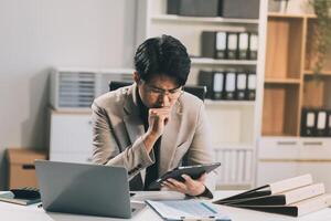 Frustrated Asian young businessman worker working on table in office. Busy employee worker people feel tired and headache from late work and overwork job document on computer desk at company workplace photo