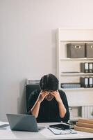 Frustrated Asian young businessman worker working on table in office. Busy employee worker people feel tired and headache from late work and overwork job document on computer desk at company workplace photo