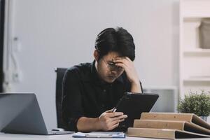 Frustrated Asian young businessman worker working on table in office. Busy employee worker people feel tired and headache from late work and overwork job document on computer desk at company workplace photo