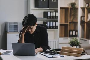 Frustrated Asian young businessman worker working on table in office. Busy employee worker people feel tired and headache from late work and overwork job document on computer desk at company workplace photo
