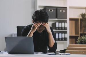 Frustrated Asian young businessman worker working on table in office. Busy employee worker people feel tired and headache from late work and overwork job document on computer desk at company workplace photo